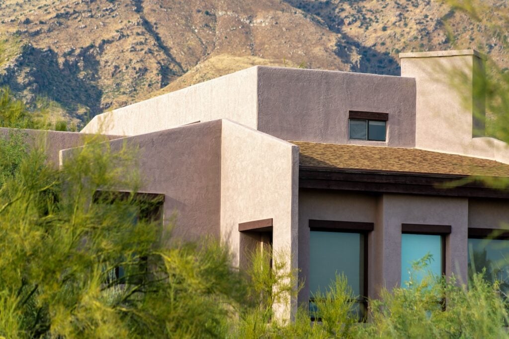 Adobe style house with flat roof and block features with visible windows and chimneys in the late afternoon sun and shade