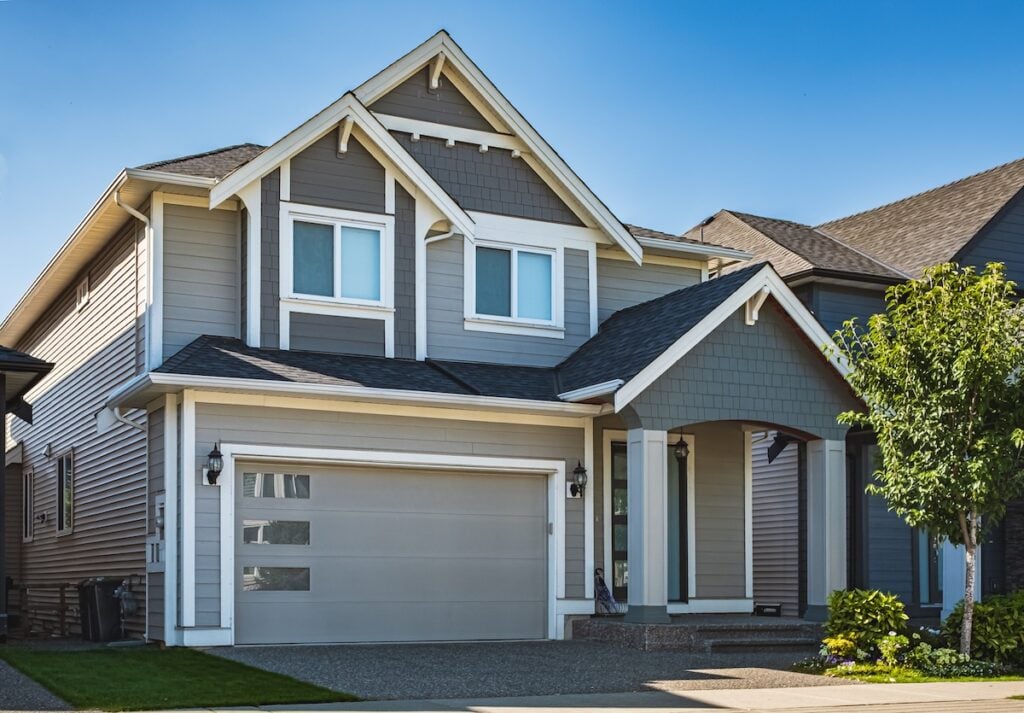 Real Estate Exterior Front House on a sunny day. Big custom made luxury house with nicely landscaped front yard and driveway to garage in suburbs. Modern designed home, New construction home exterior