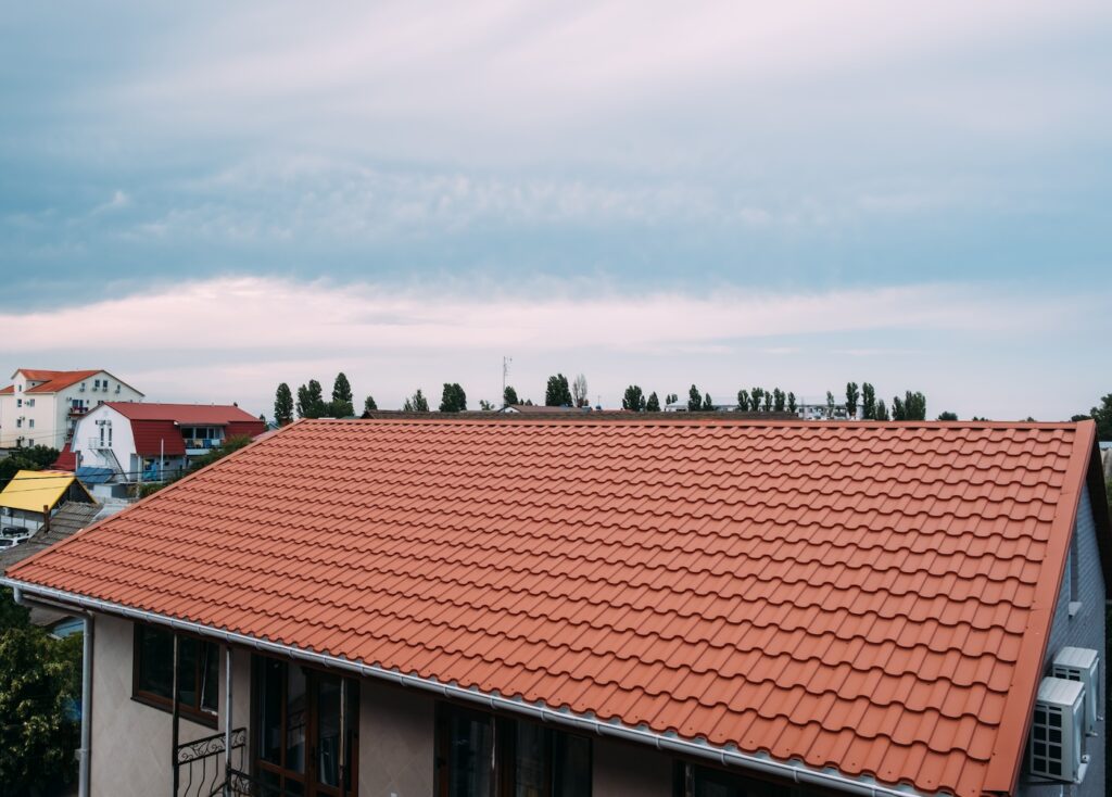 View of the roof of the house with brown metal tiles. Summer day.
