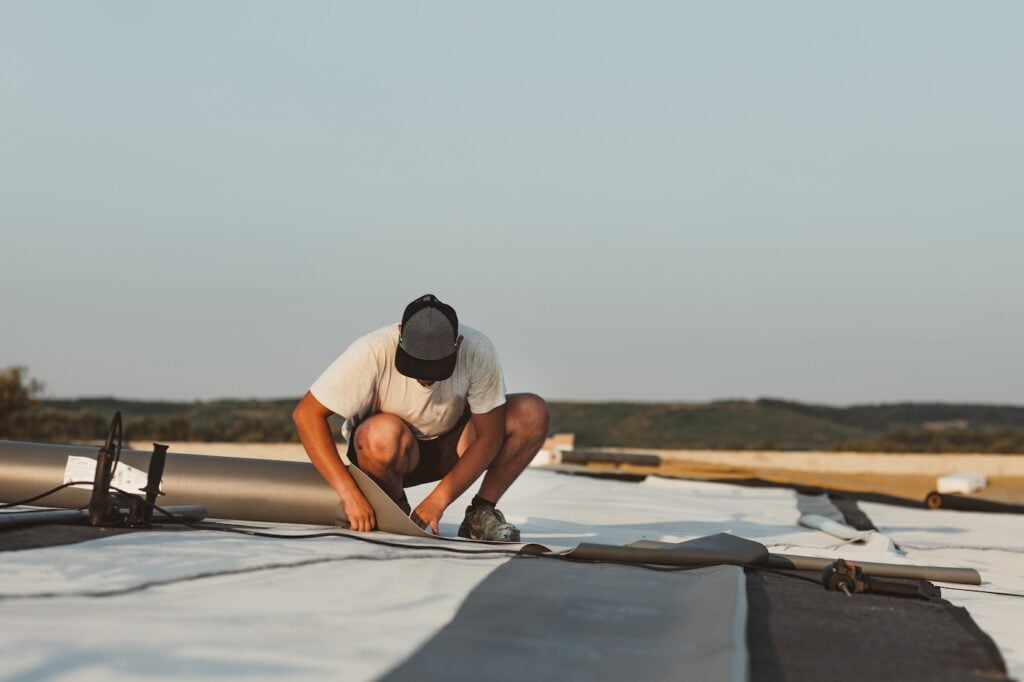 Worker applies pvc synthetic membrane roller on roof