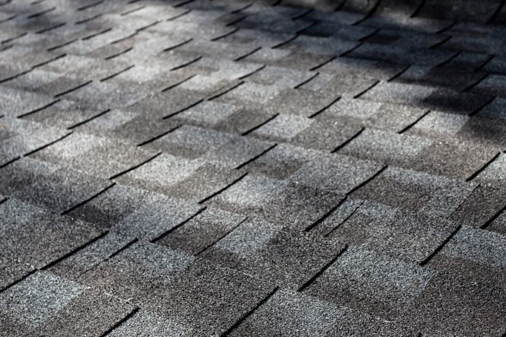 close-up of an asphalt shingle roof at an angle with dappled sunlight