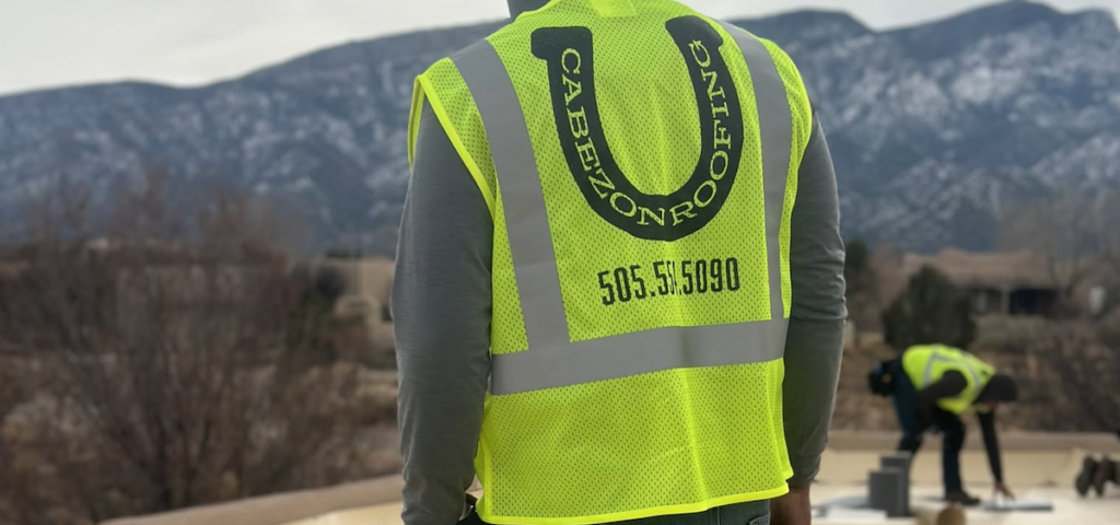 Roofing crew wearing Cabezon Roofing safety vests working on a flat roof in Albuquerque