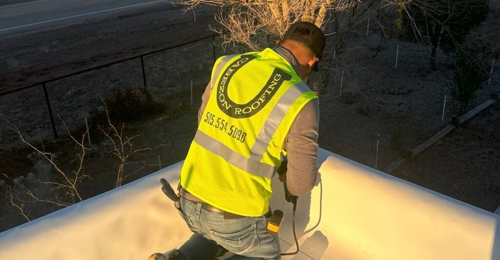 Cabezon Roofing technician wearing a safety vest working on a flat roof at sunset